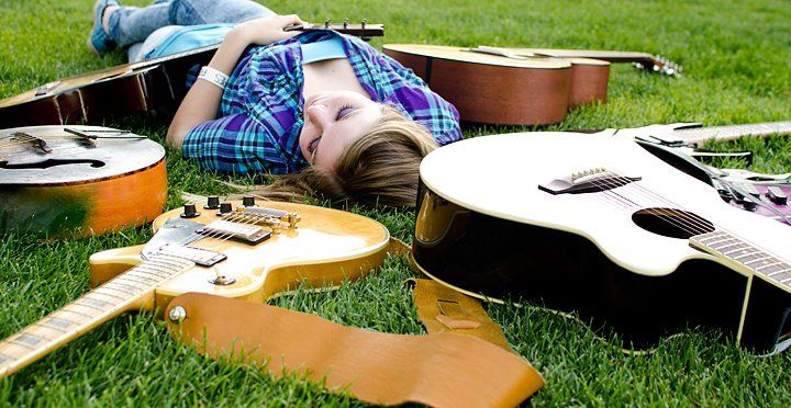 Musical instruments including guitars lay scattered on green grass in warm sunlight.
