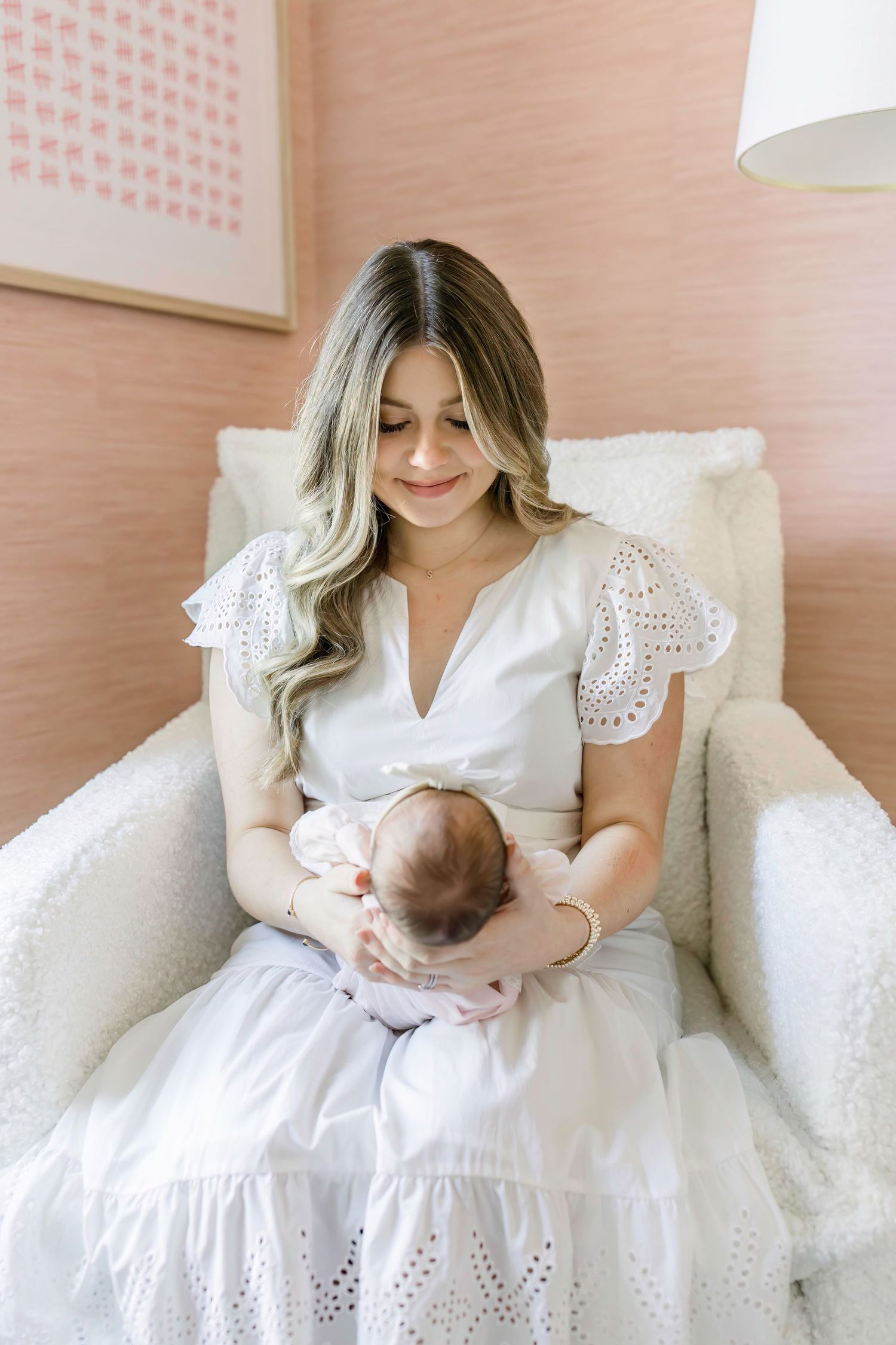 Intimate moment in a pink nursery with white eyelet dress and natural window light.