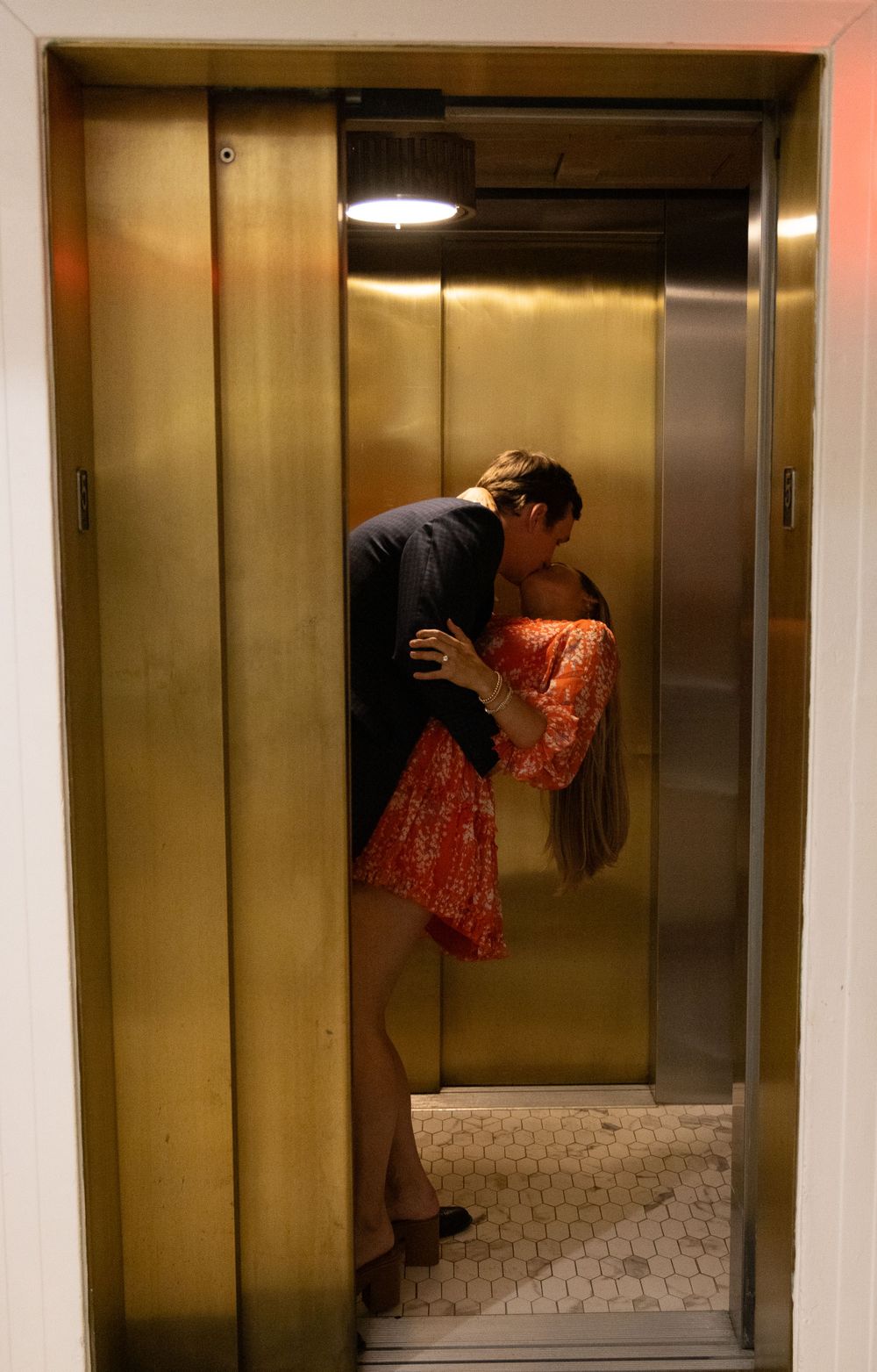A romantic couple sharing an intimate moment together in a golden-lit elevator after engagement.