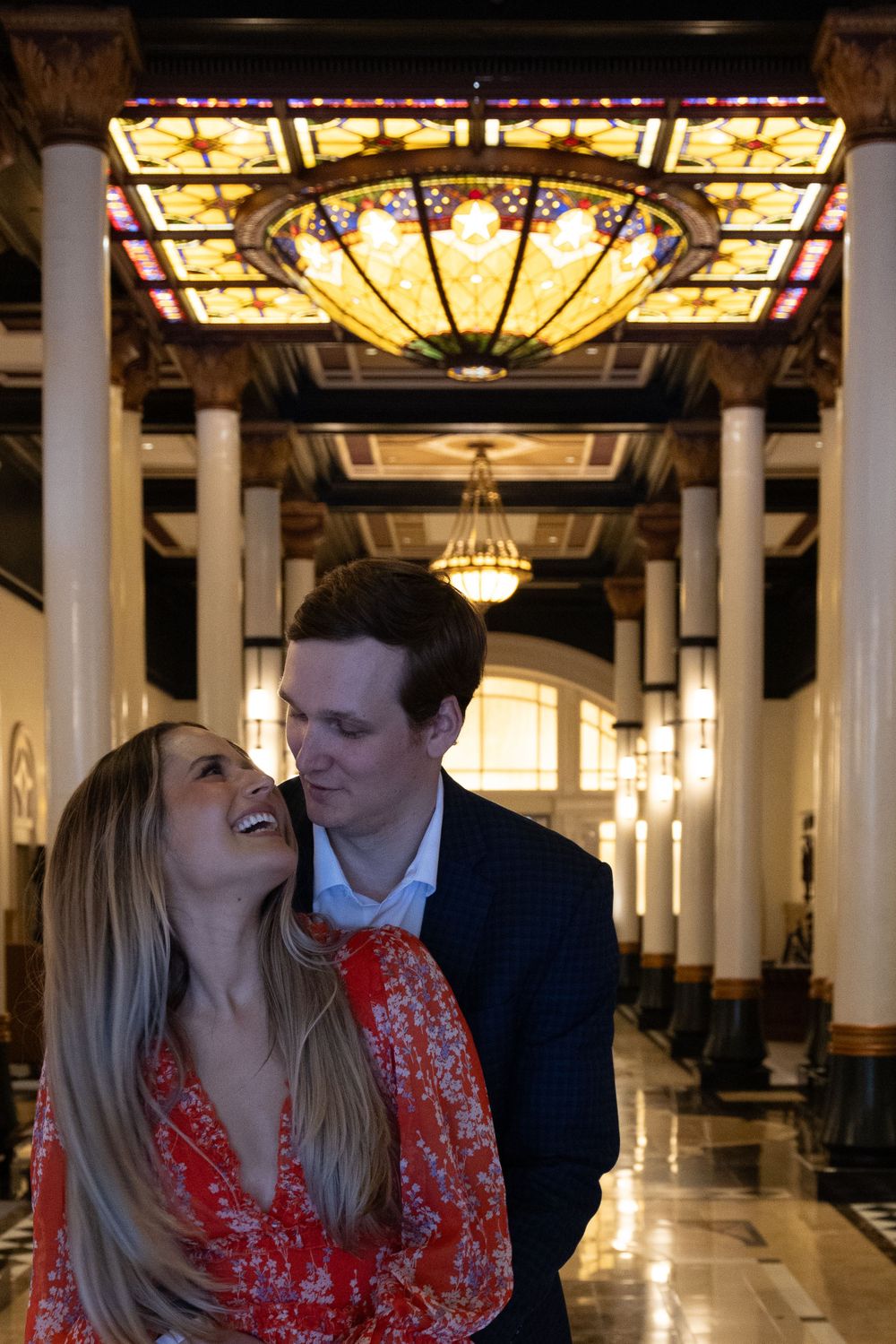 Romantic moment under ornate stained glass ceiling in historic hallway.