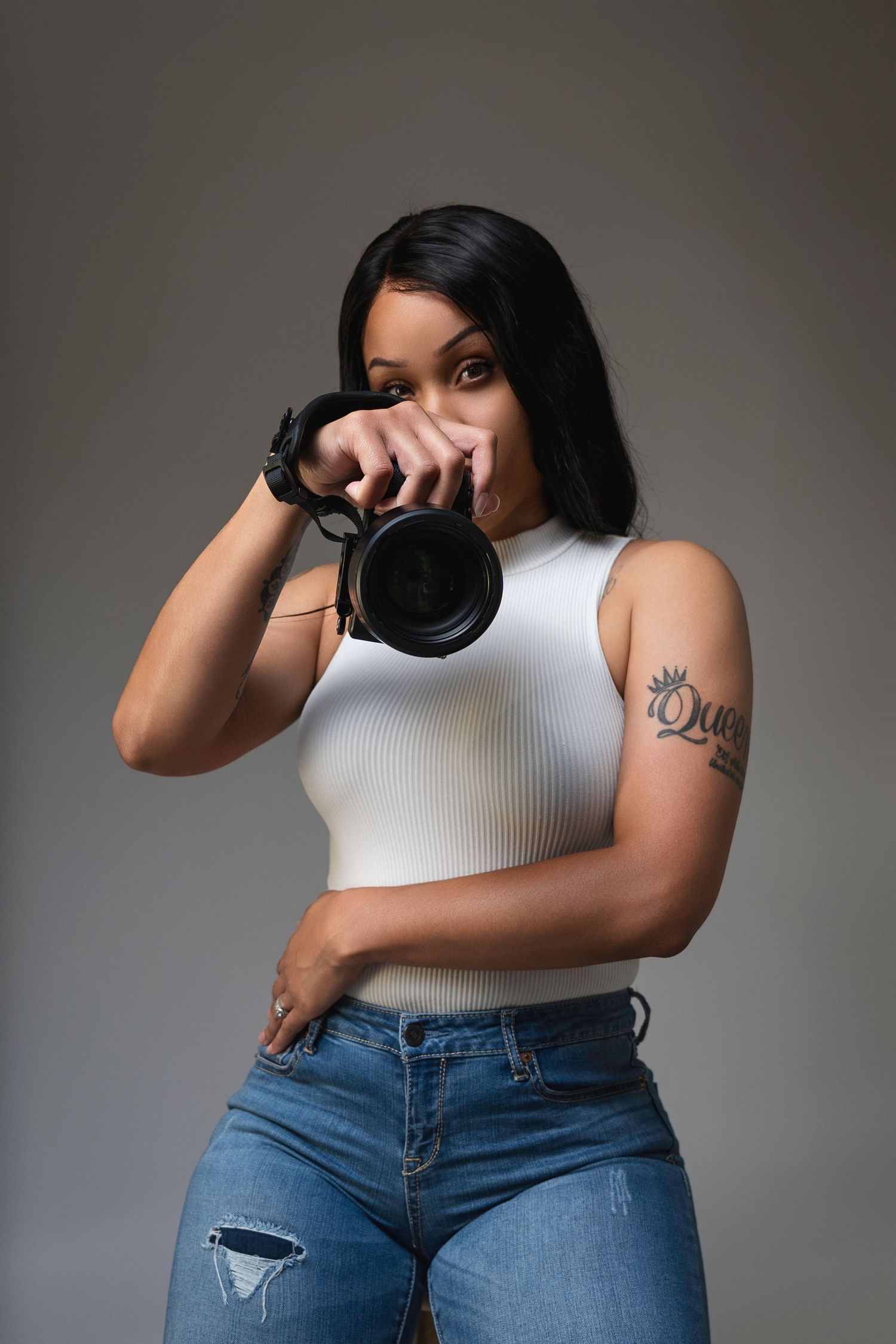 Photographer holding a professional camera with lens up to their eye while wearing a beige top.