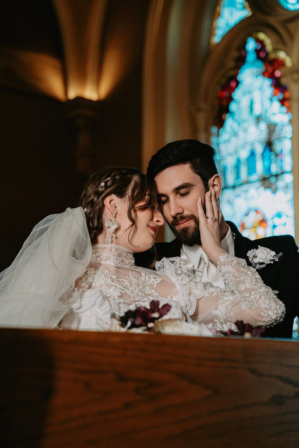 Romantic wedding couple shares intimate moments in a church with stained glass windows casting blue light.