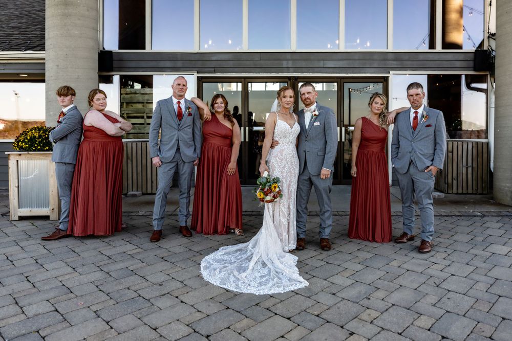 Wedding party poses outdoors with bridesmaids in burgundy dresses and groomsmen in gray suits.