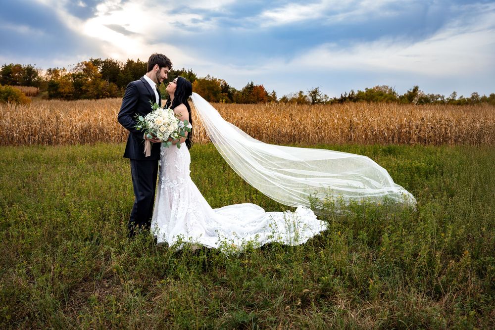A flowing white wedding dress veil catches the breeze across a golden autumn field at sunset.