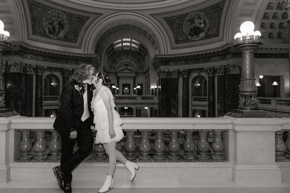 Black and white photo of a couple kissing in an elegant domed building interior with ornate columns.