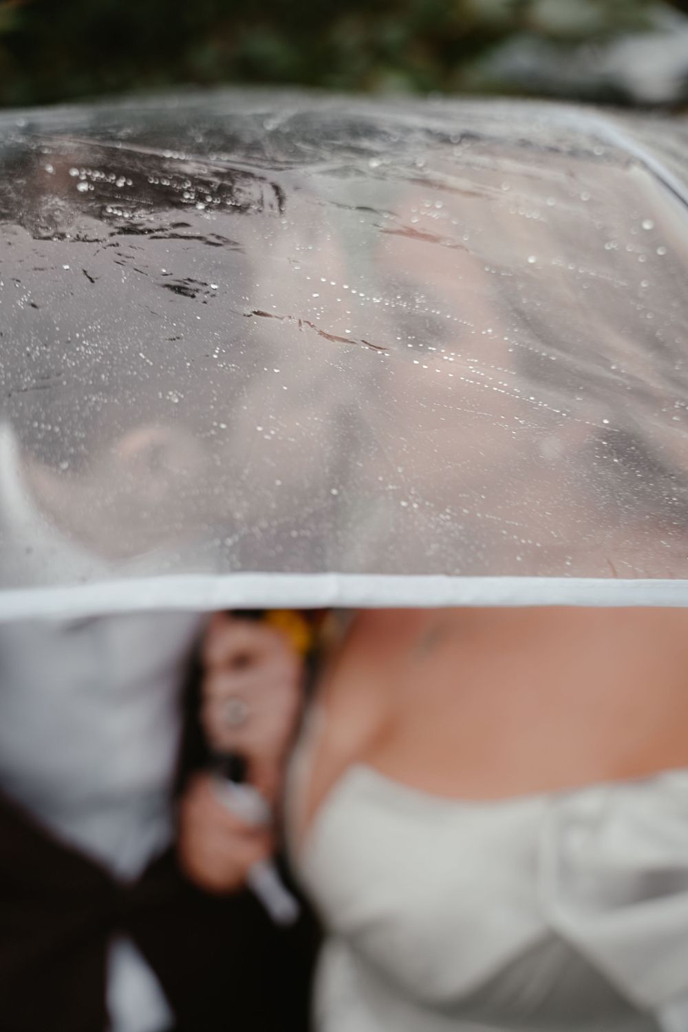 Artistic wedding photo through rain-covered transparent surface.