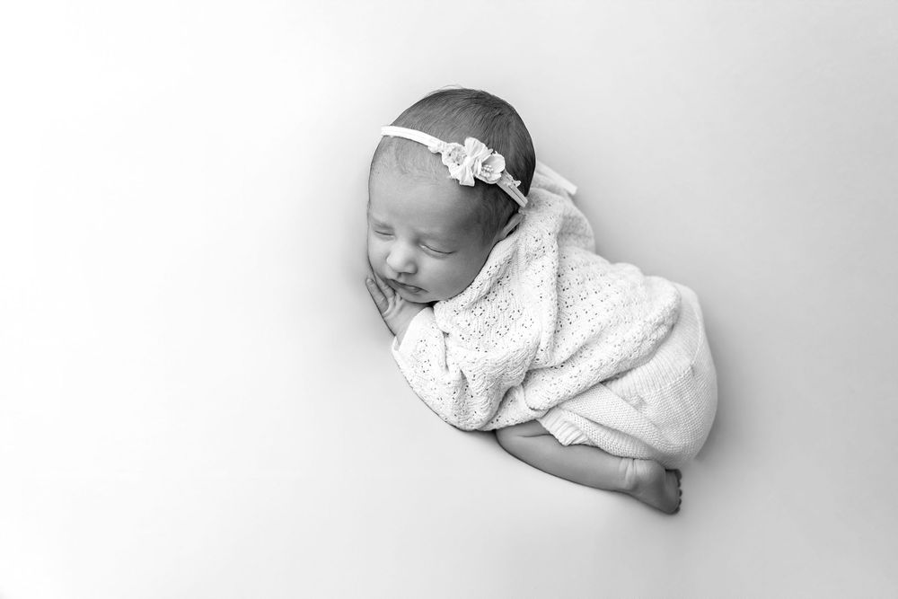 A sleeping newborn baby wrapped in white cloth lies peacefully against a light gray background.