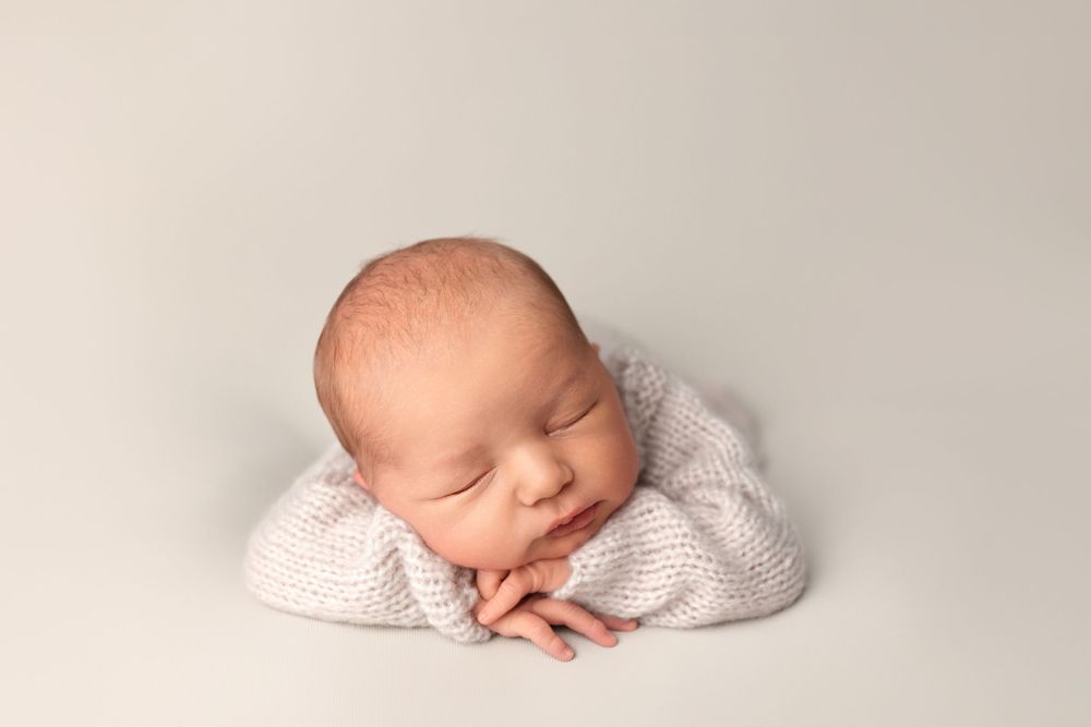 Serene portrait of sleeping newborn in white knit sweater.