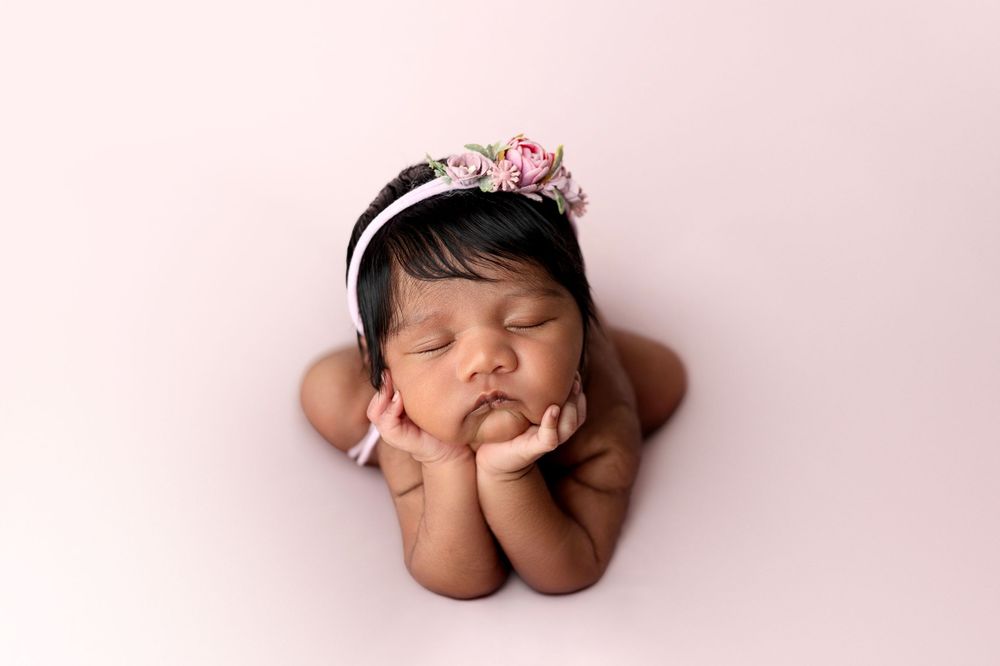 A sleeping newborn baby in pink tones curled up in a fetal position during a professional photography session.