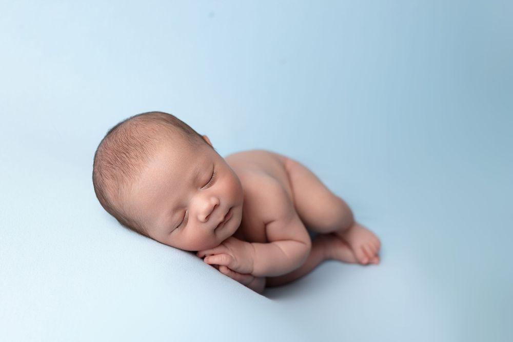A sleeping newborn baby photographed in a light blue background with soft lighting.