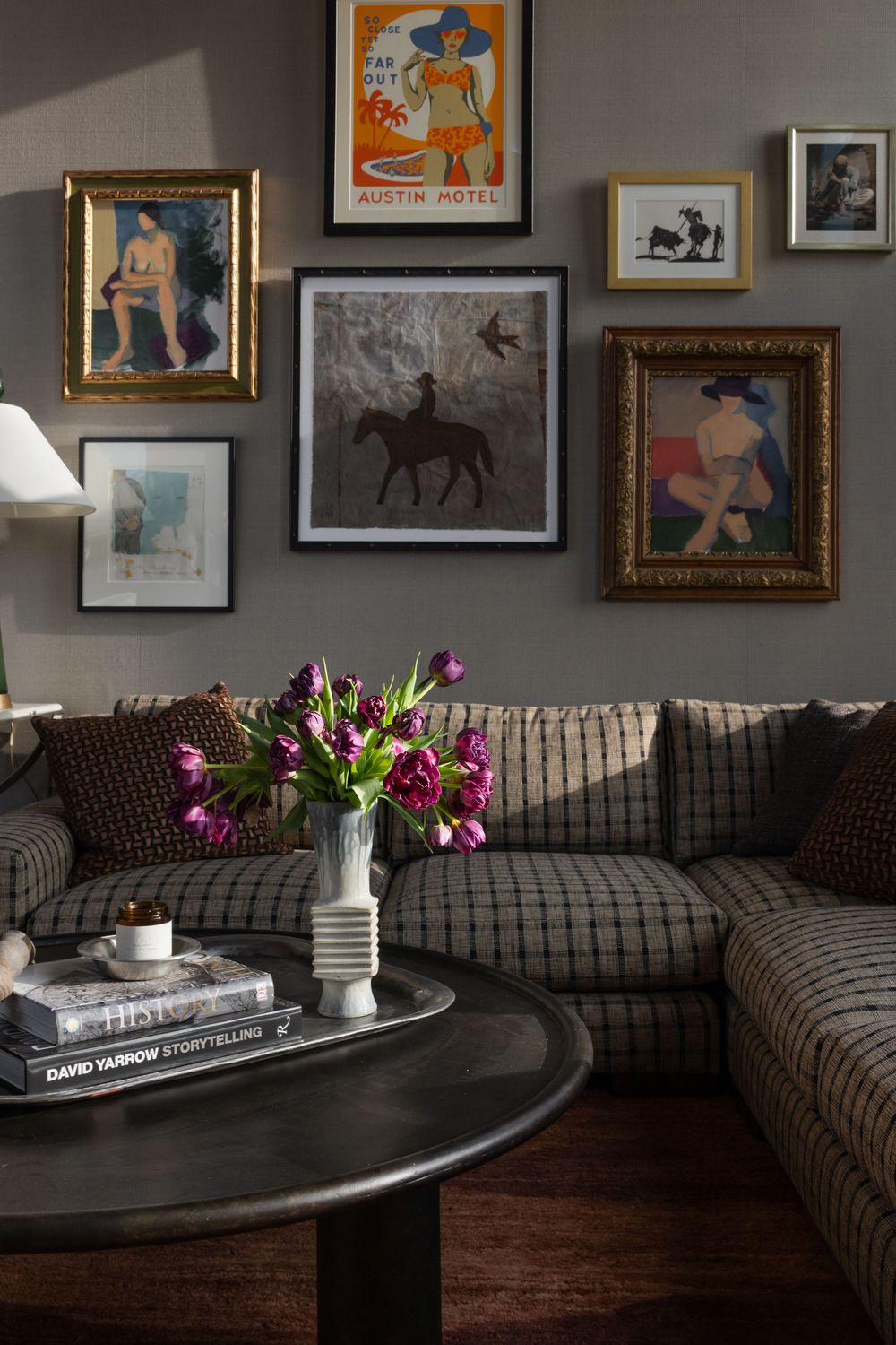 Cozy living room with plaid sectional sofa, gallery wall art, purple tulips in vase, and dark coffee table with books.