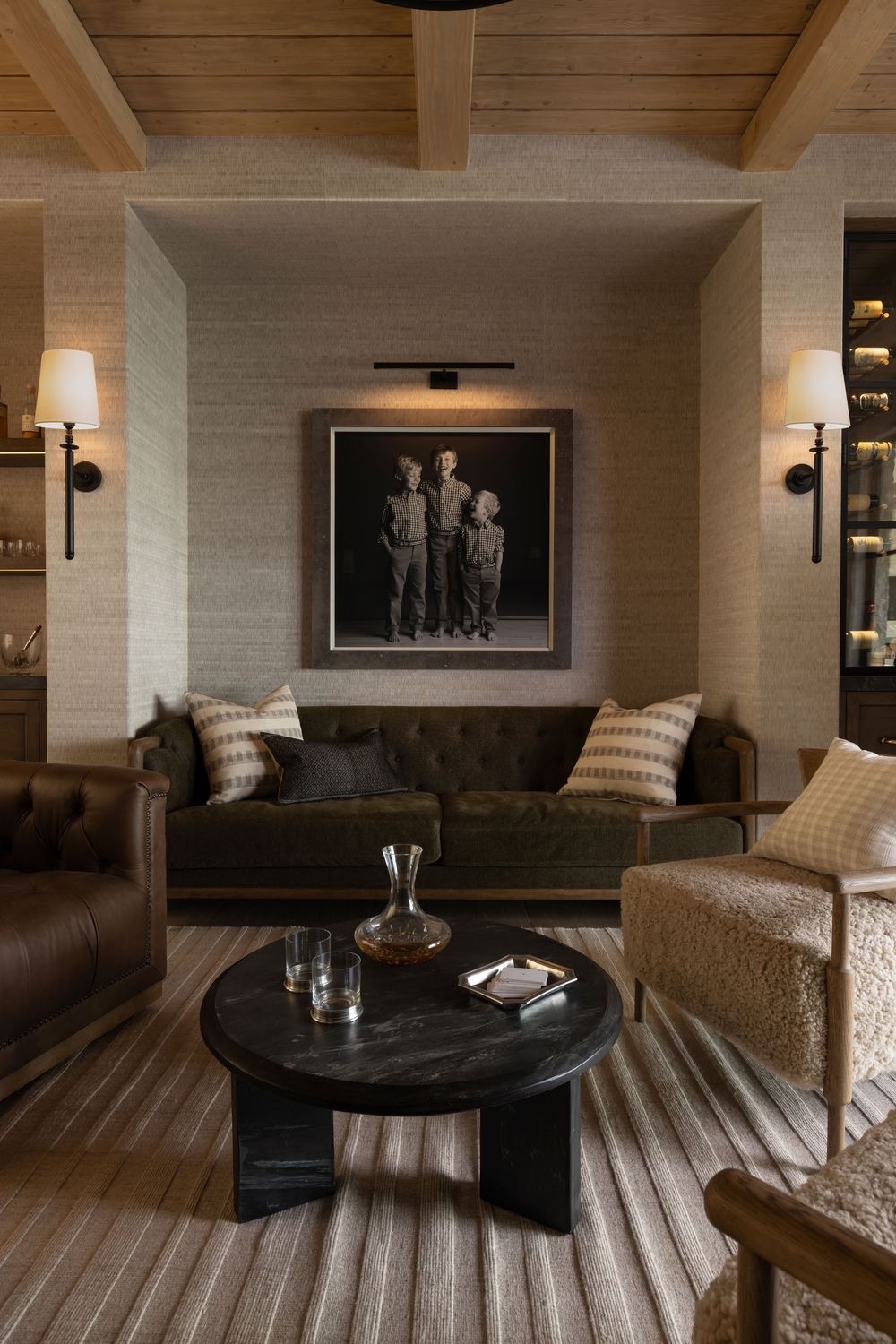 Cozy living room with tufted leather sofas, round black coffee table, striped rug, wall sconces, and vintage black-and-white photo art.