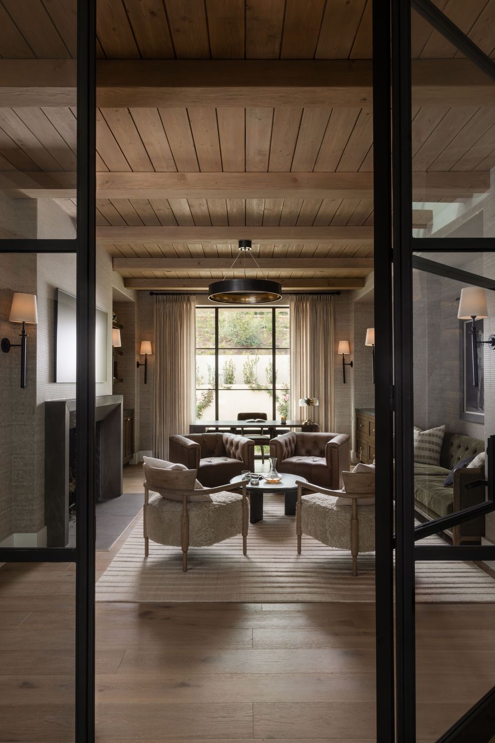 Elegant living room with wood ceiling, woven armchairs, glass doors, and large window in warm neutral tones.