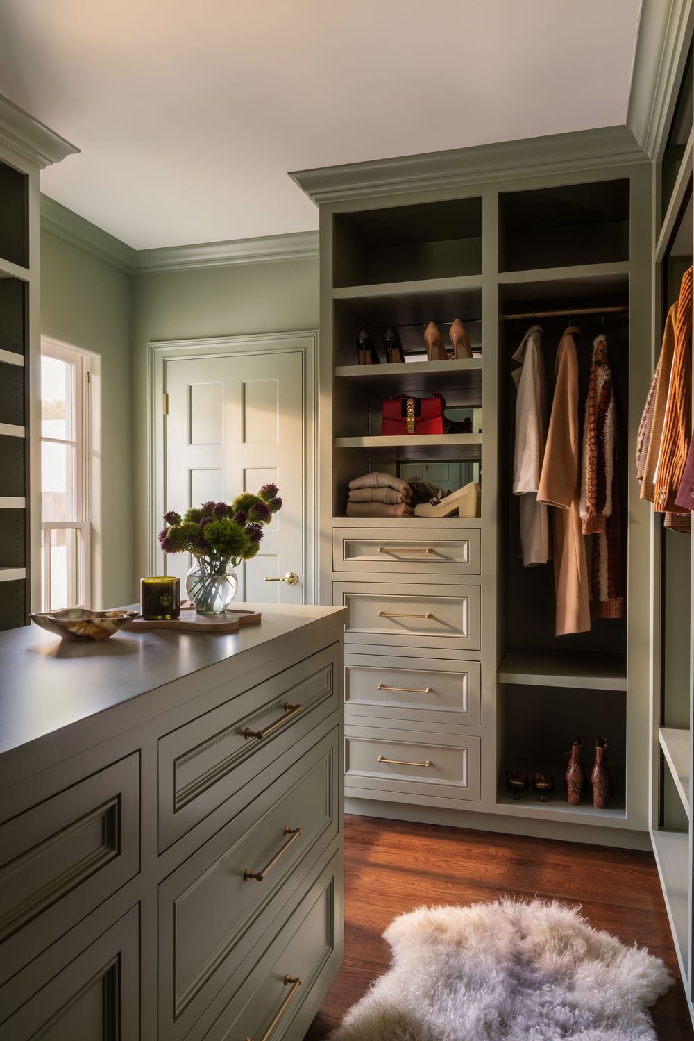 Elegant walk-in closet with sage green cabinetry, gold hardware, built-in shelving, hanging space, and hardwood floors.
