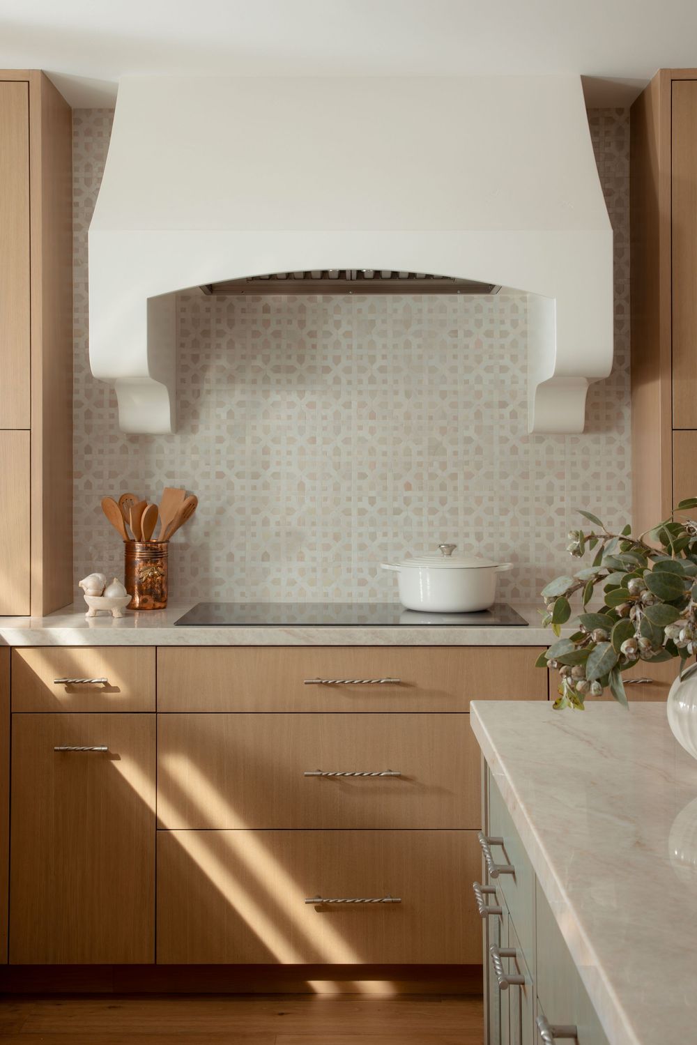 Modern kitchen interior with beige cabinets, marble countertops, white tile backsplash and natural light streaming in.