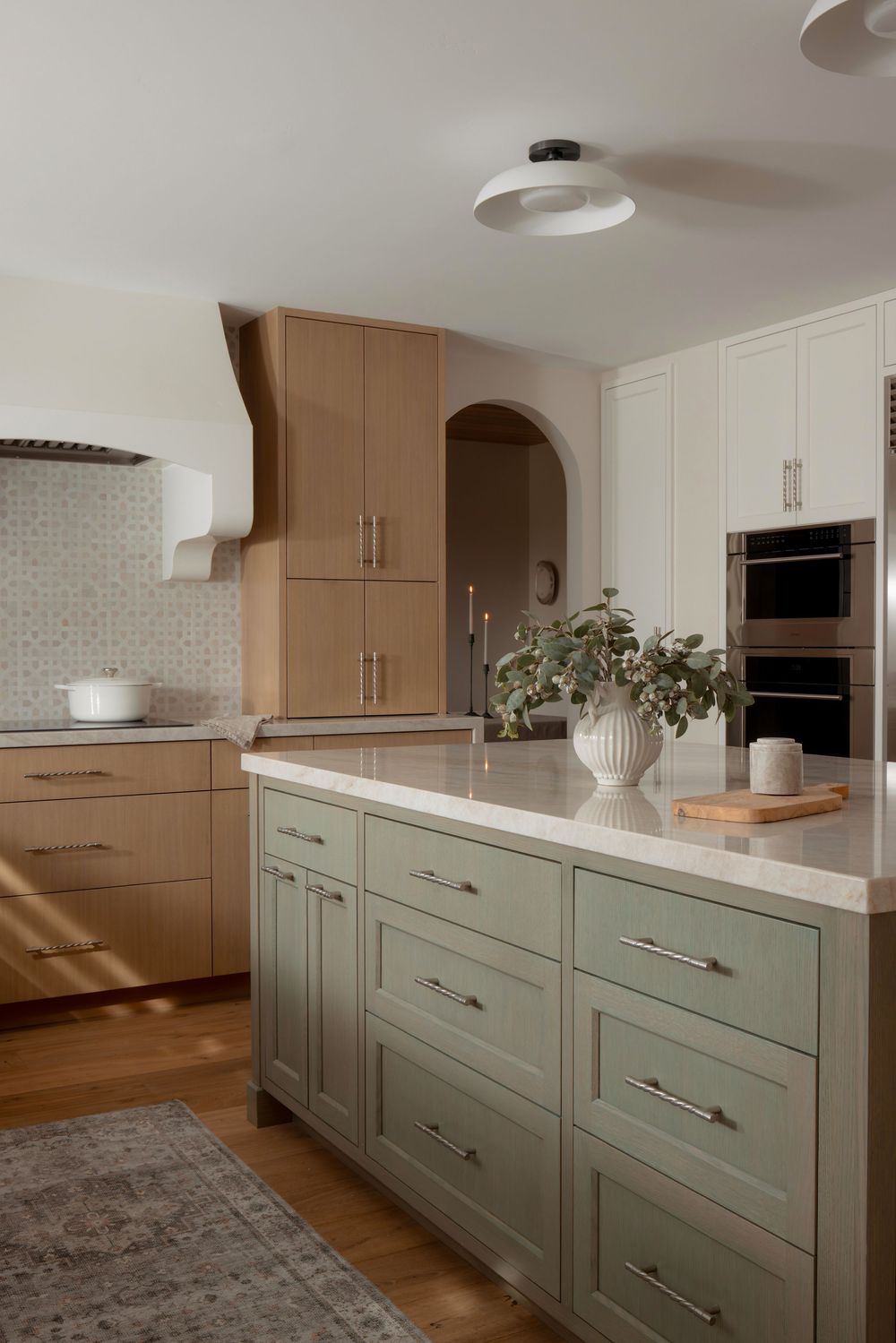 Modern kitchen features two-tone cabinetry in sage green and beige with sleek hardware and white countertops.