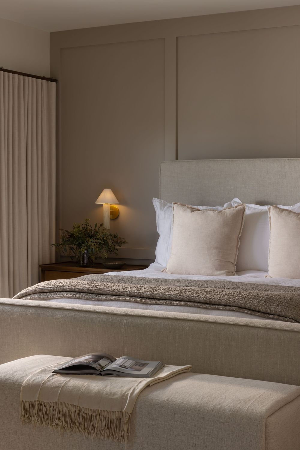 A modern minimalist hotel bedroom with neutral tones featuring white bedding and a textured throw blanket.