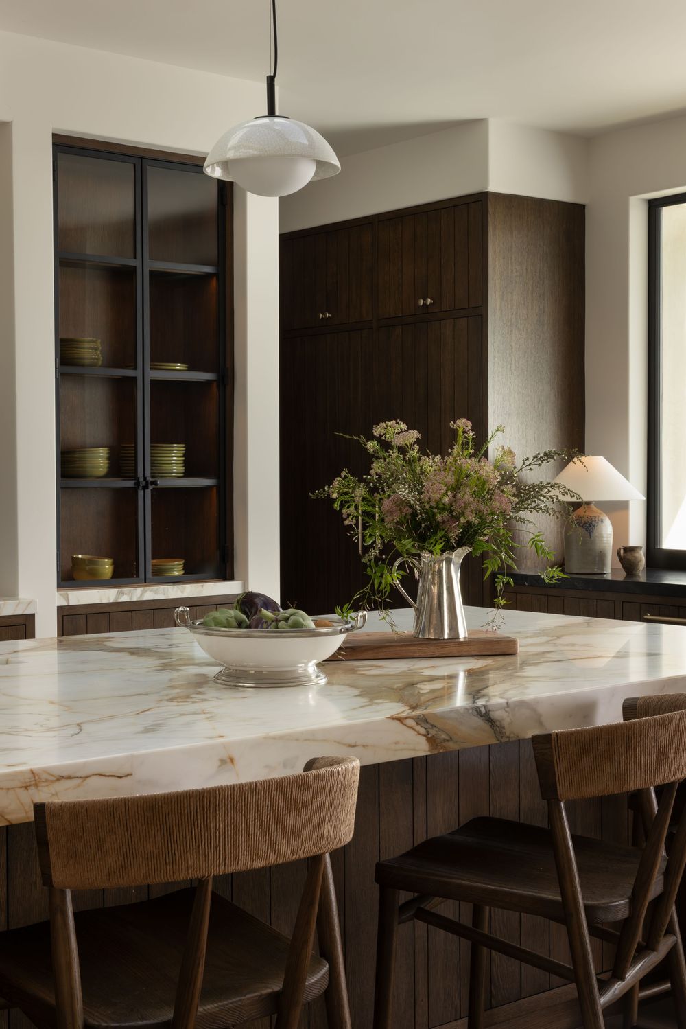 Modern kitchen interior with dark wood cabinets, white marble countertops and bar seating along an expansive island.