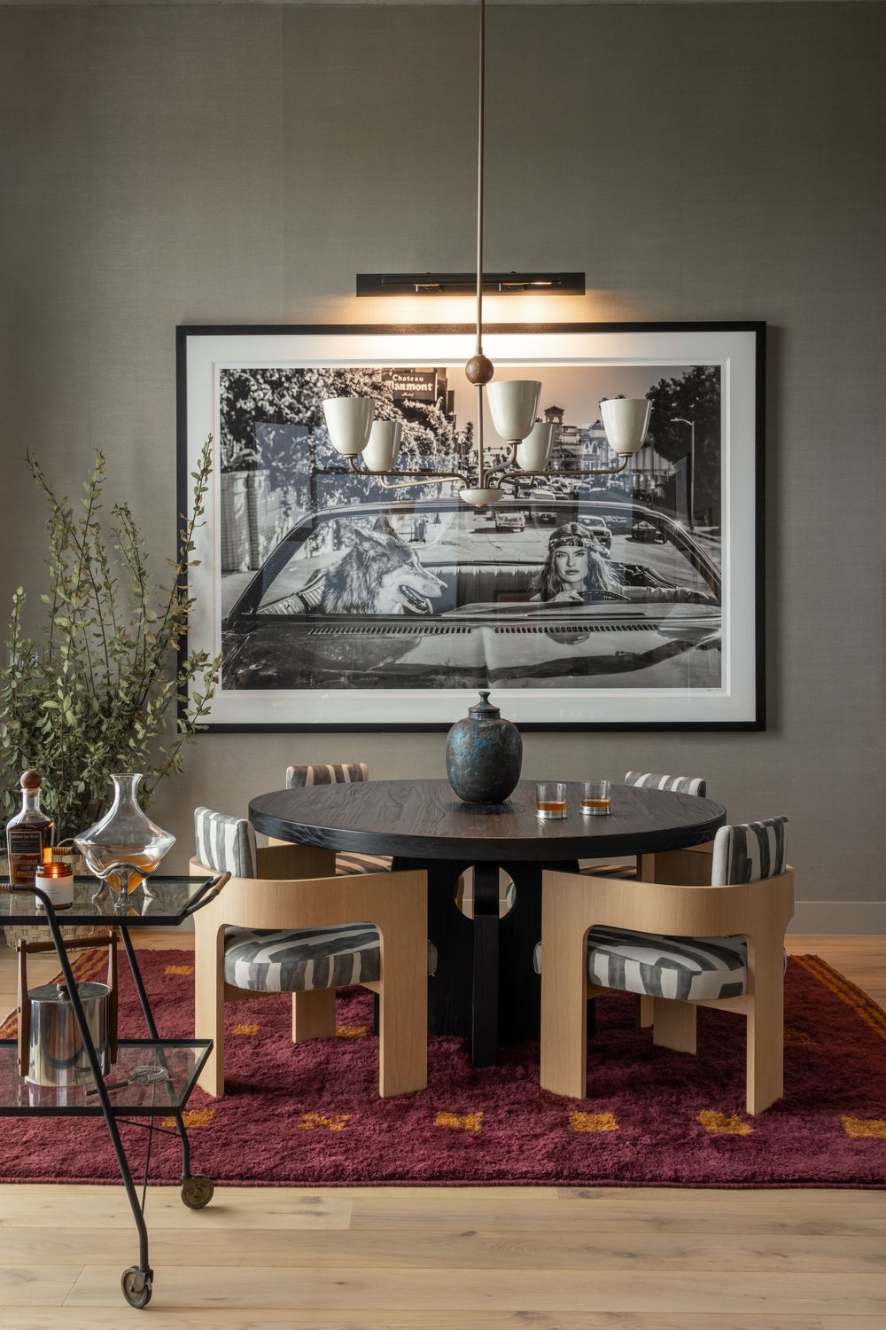 Modern dining nook with round black table, bentwood chairs, burgundy rug, and large black-and-white photo art on gray wall.