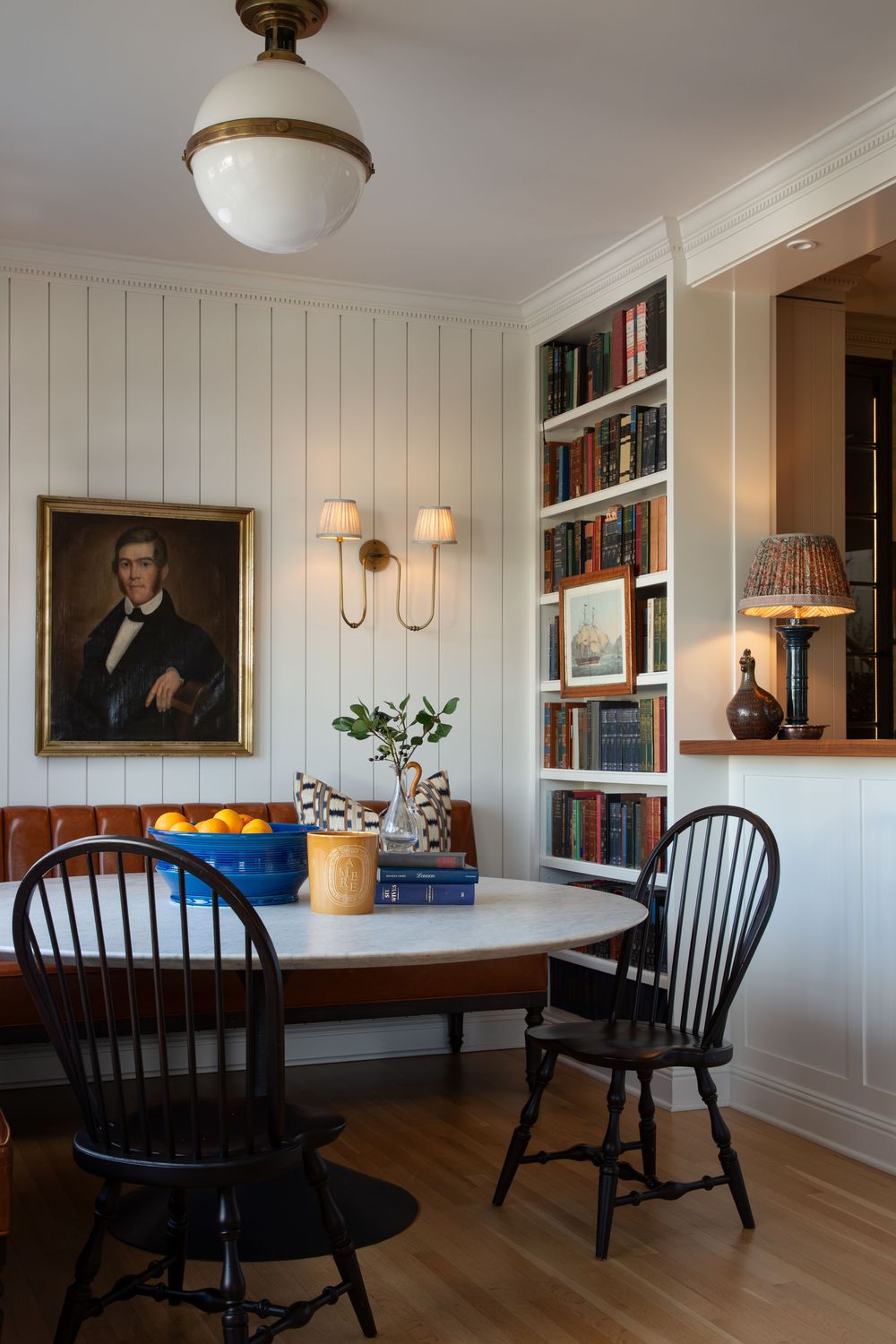 A panoramic view of a traditional dining room with white walls, wood floors, and black Windsor chairs.