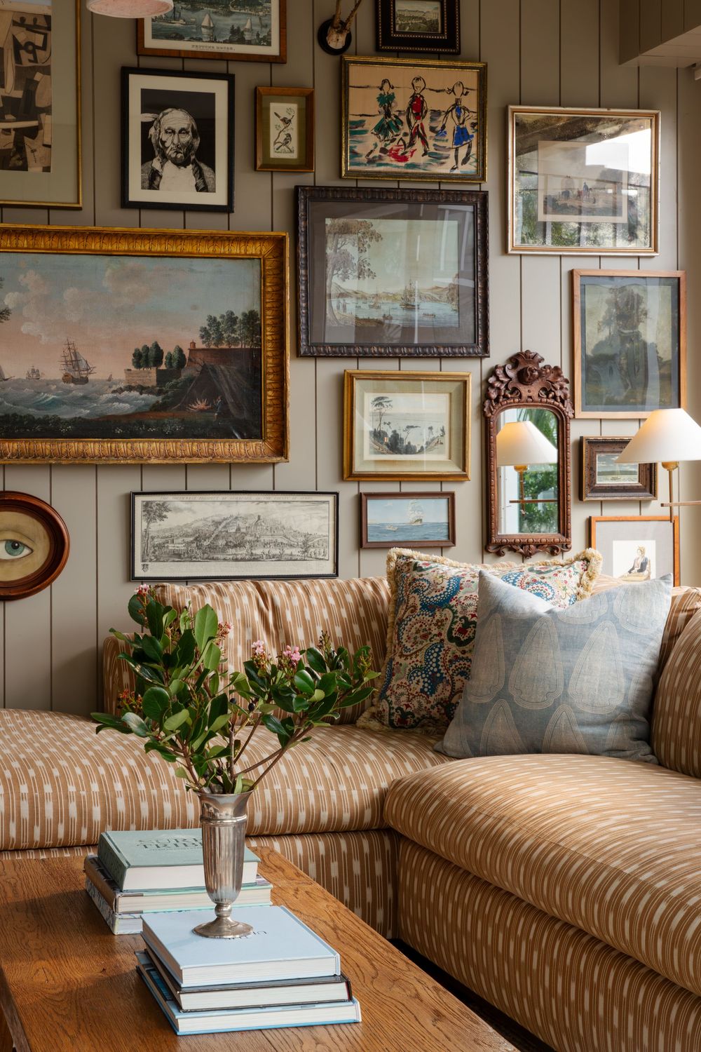 A cozy living room with striped beige couch, gallery wall of framed artwork, and decorative throw pillows and plants.