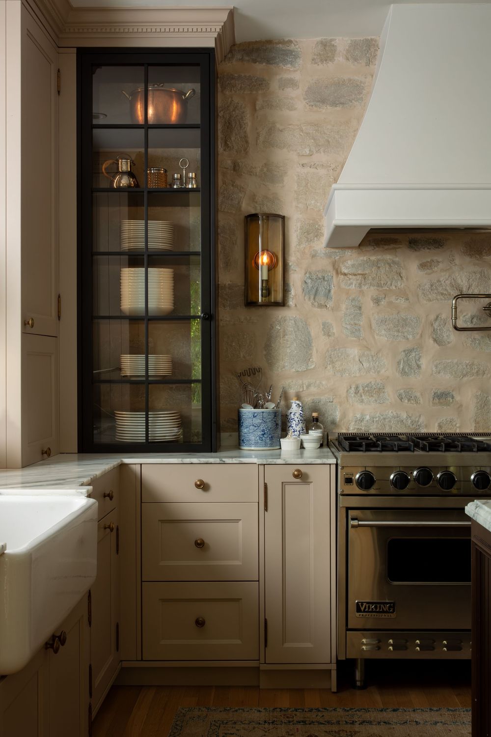 Modern kitchen with exposed stone walls, dark wood cabinets, and stainless steel appliances in warm lighting.