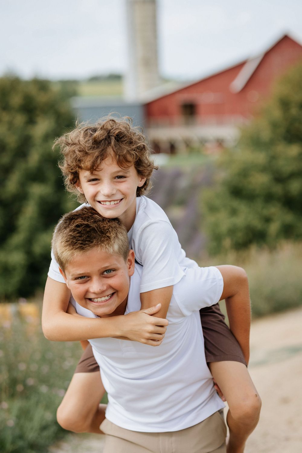 Playful piggyback rides and laughter near a red barn and silo on a sunny day.