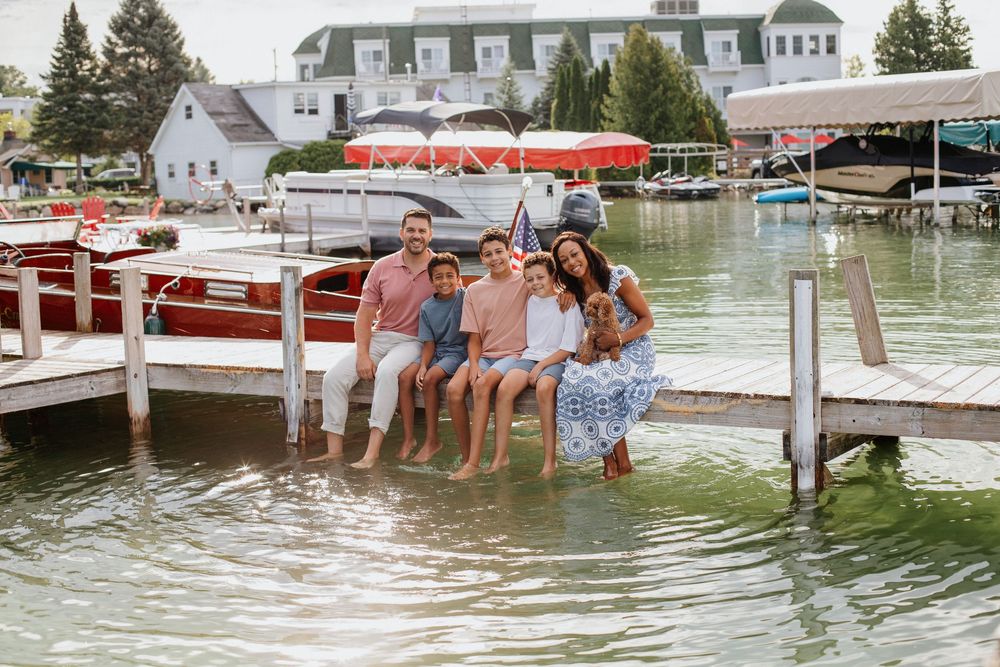 People enjoying a summer day jumping off a dock into a lake with boats and waterfront homes in the background.