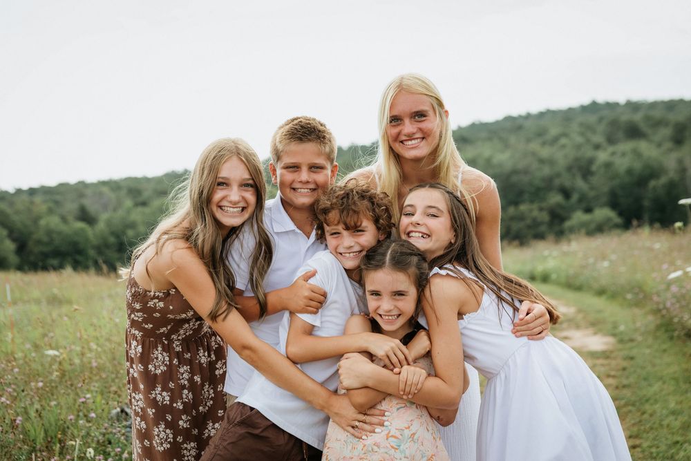 Group sharing embraces and smiles while standing in a blooming summer meadow.
