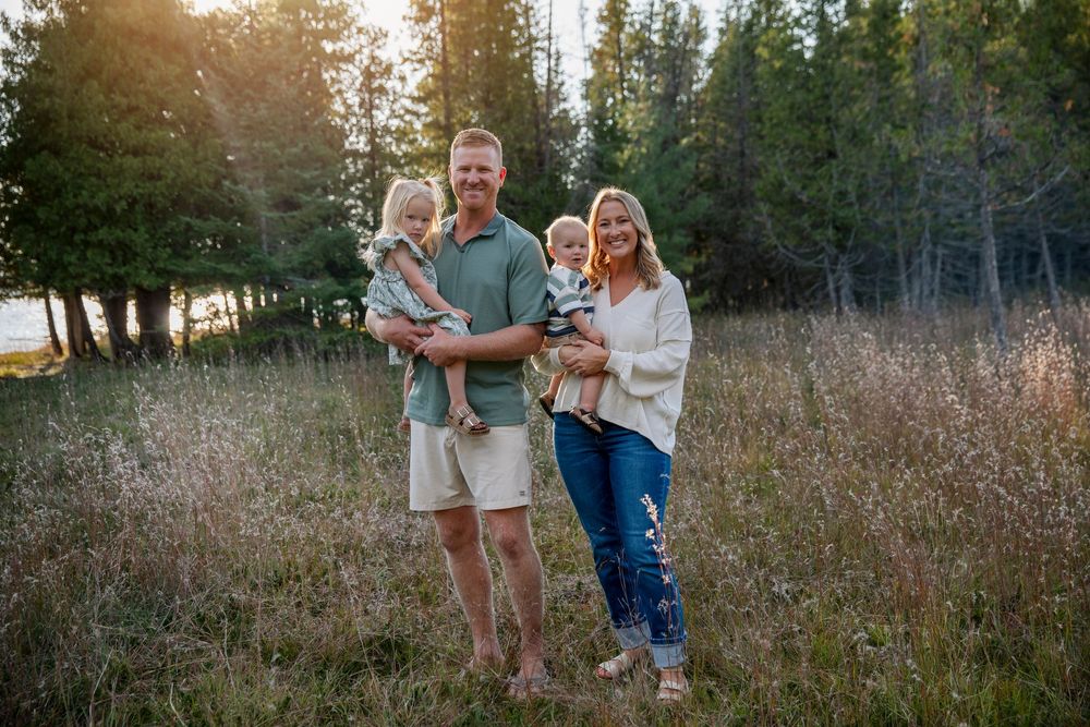 Scenic family photoshoot in natural meadow with evergreen forest backdrop.