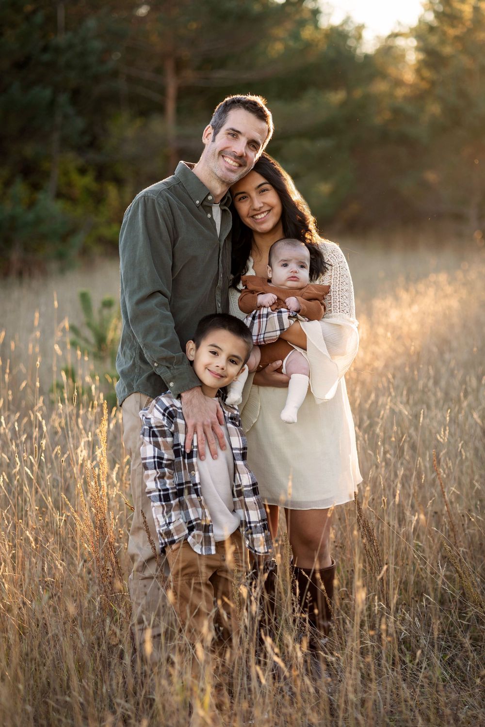 Family portrait in golden field at sunset with warm autumn lighting.