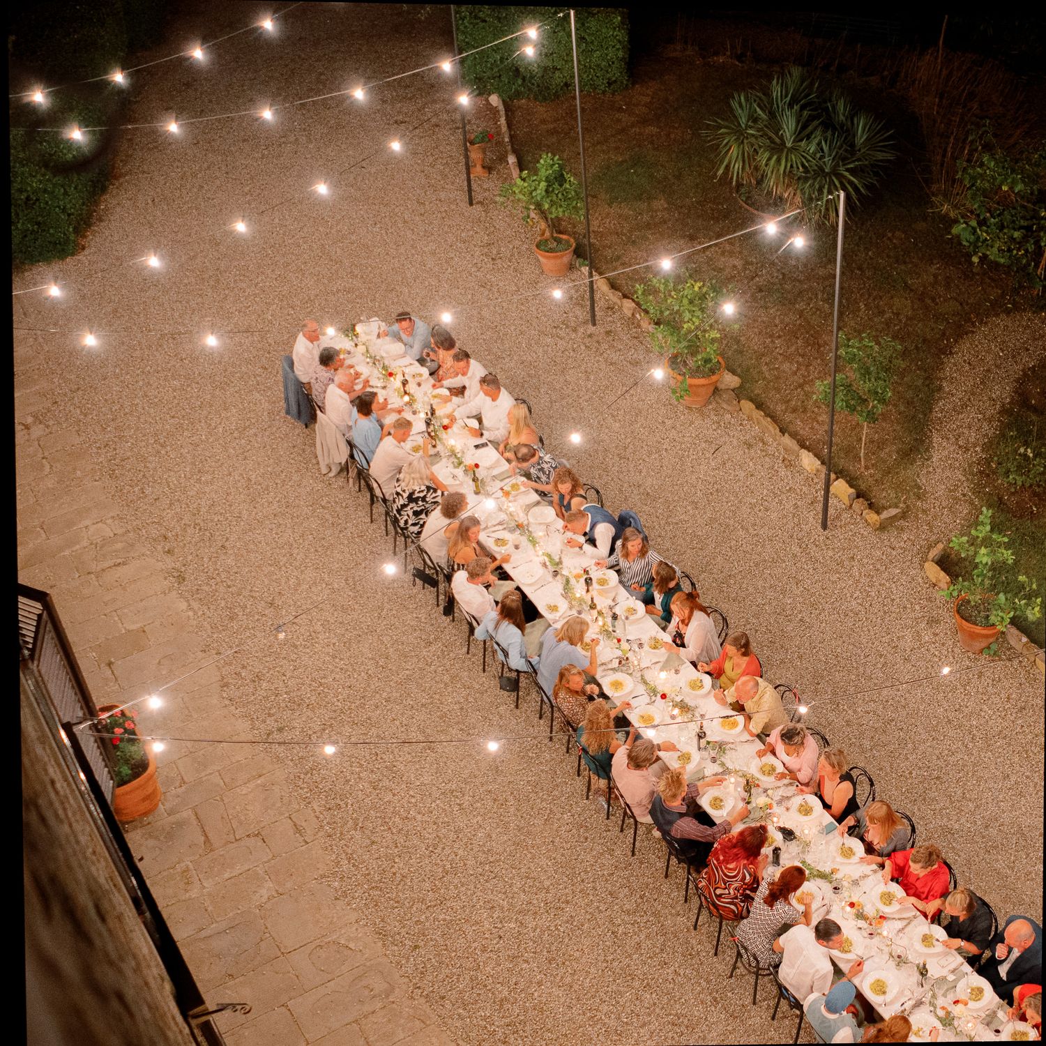 View from above of a wedding table with guests chatting and eating under the lights, at Borgo Castelvecchi