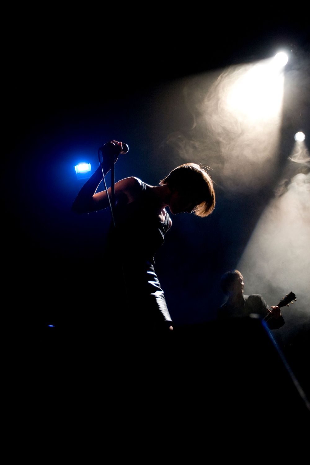 Silhouetted performer on stage with dramatic blue and white spotlights creating atmospheric backlighting.
