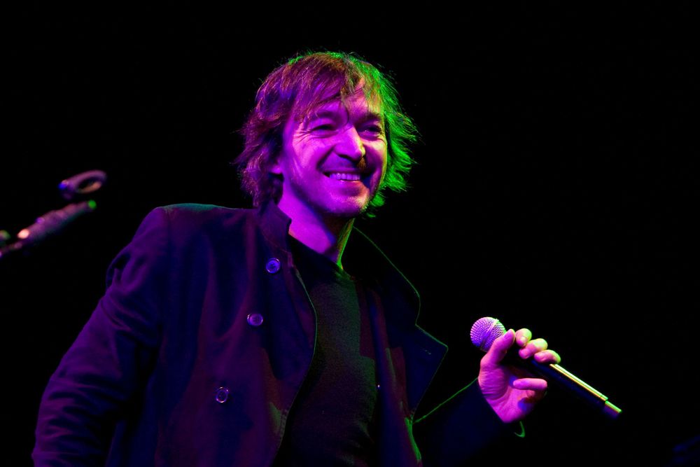 Performer sings into microphone under purple and green stage lighting.