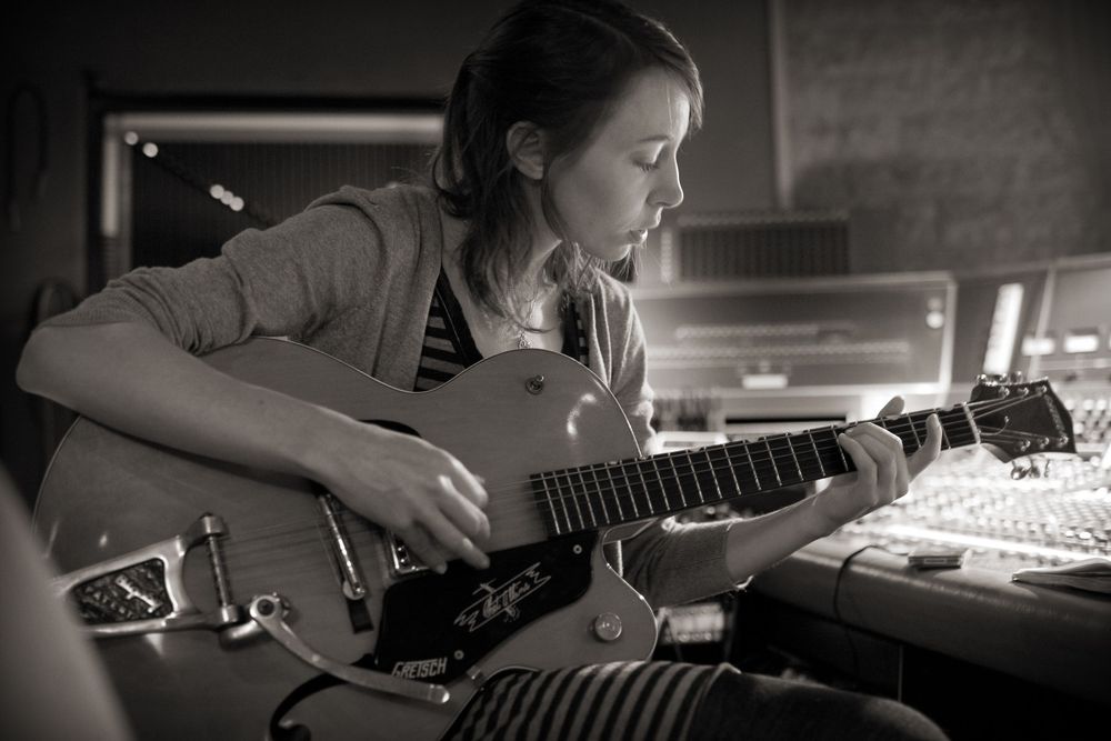Musician concentrating while playing an acoustic guitar in a recording studio setting.