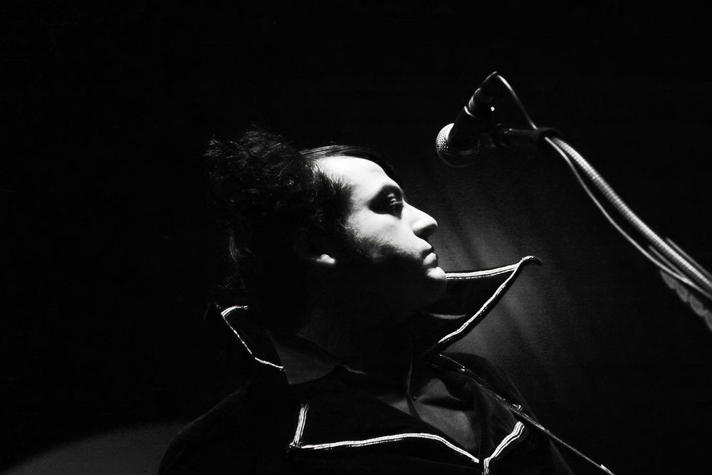 Close-up profile shot of a vocalist performing in dramatic black and white stage lighting.