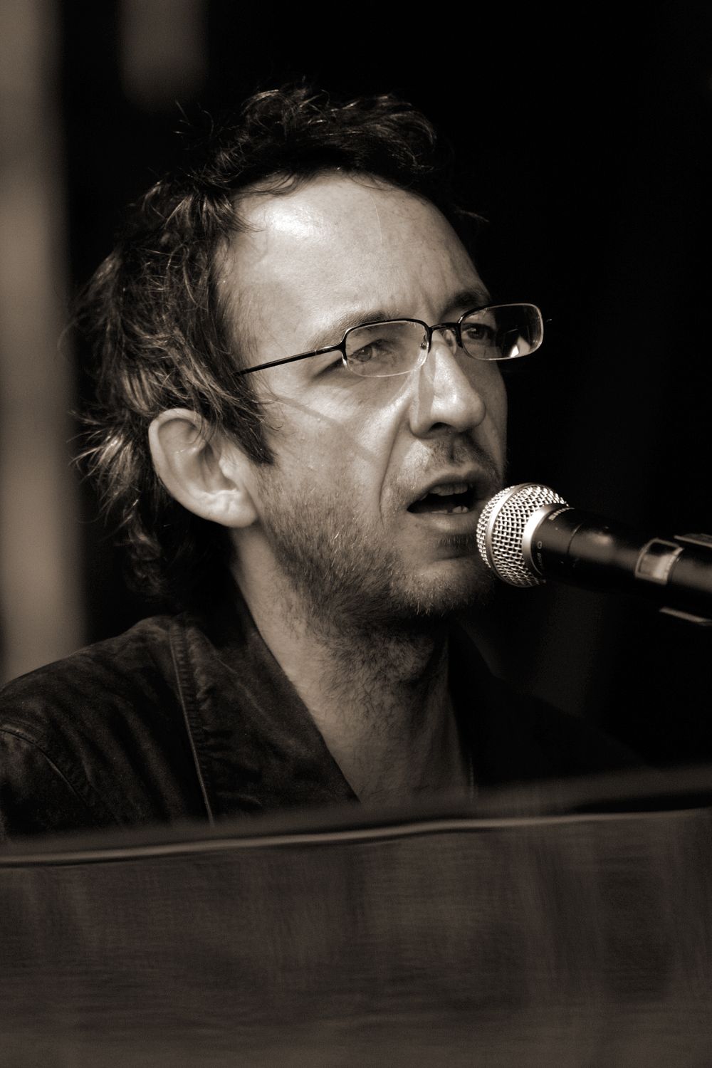 Close-up performance shot of musician singing at microphone in sepia tones.