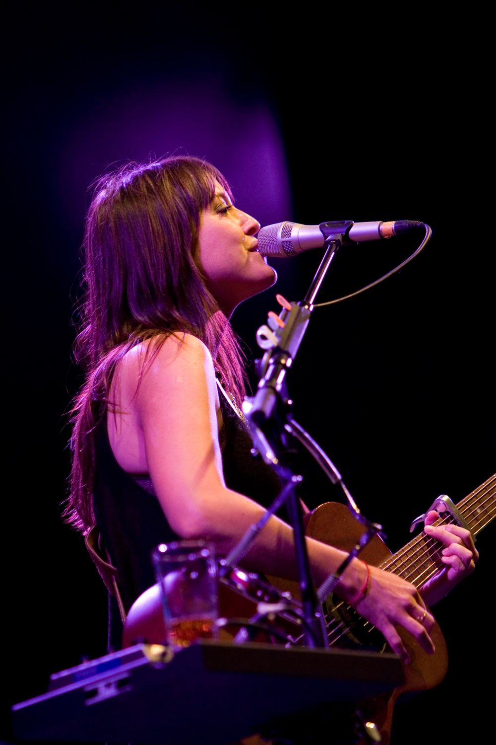 Musician playing guitar and singing into microphone under purple stage lighting.