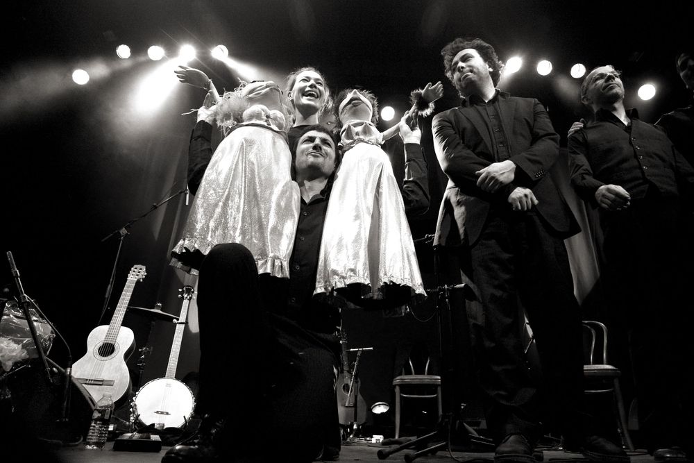 Group performance on stage featuring figures in white costumes with acoustic guitars.