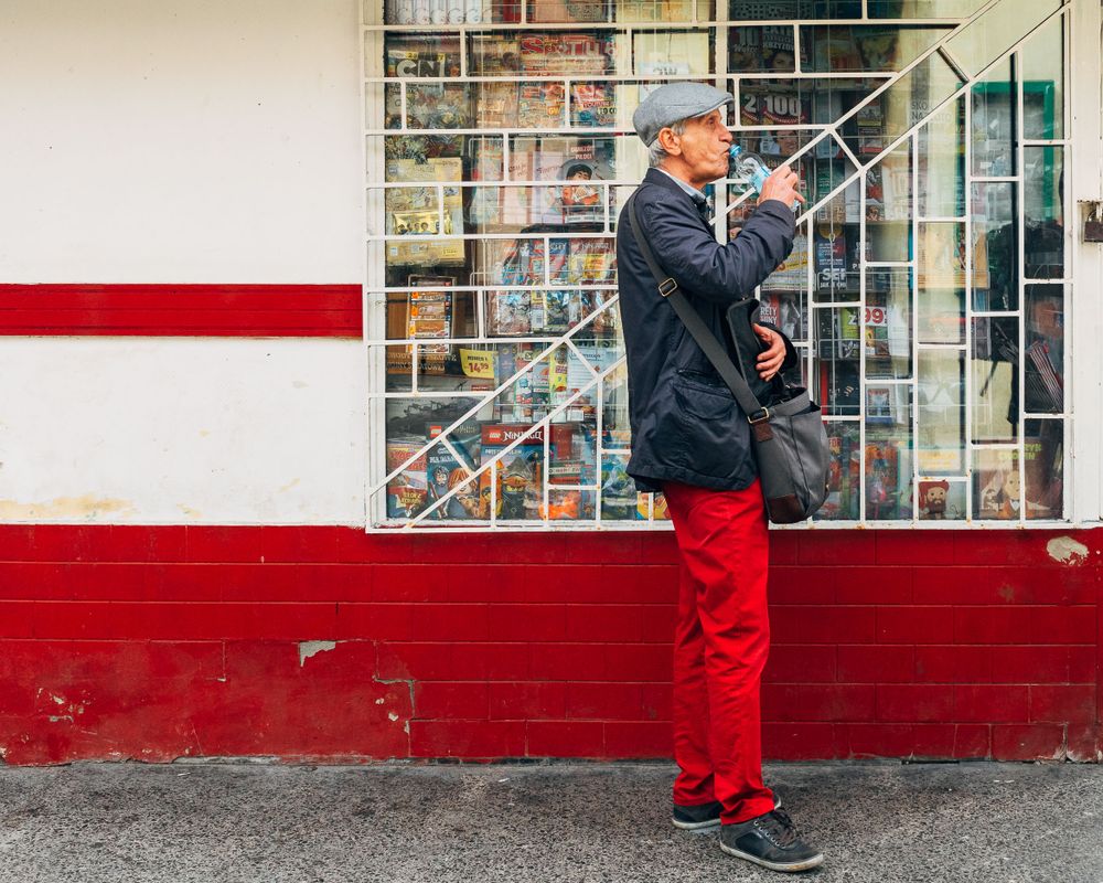 Person in red pants walking along white building wall with red stripe.