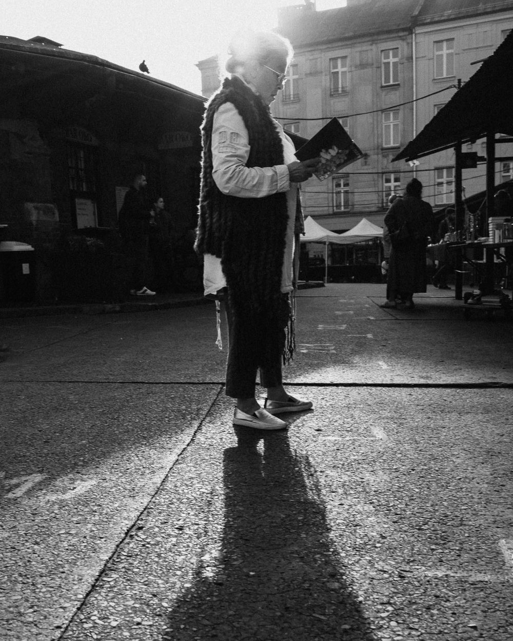 Dramatic black and white street scene with long shadows cast on cobblestone ground.