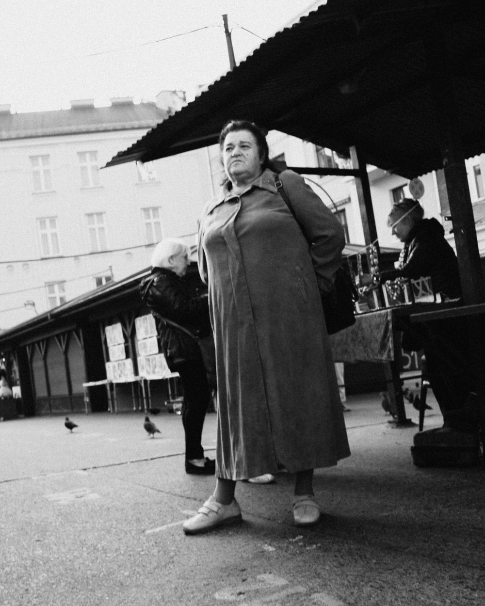 Black and white street photography of a person sitting under a market umbrella.