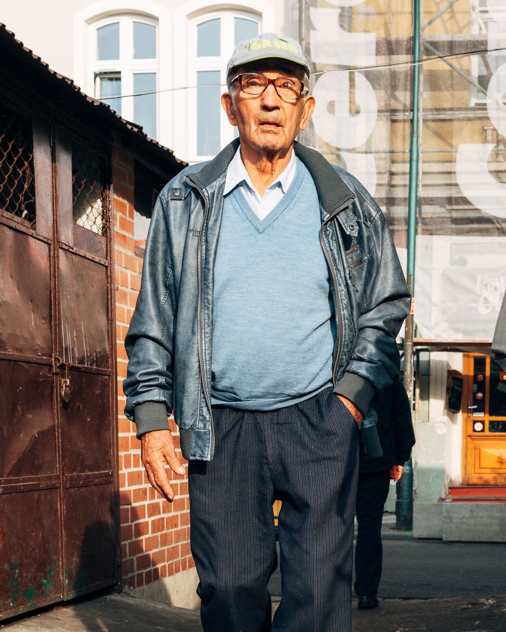 Elderly person in casual attire standing against an urban backdrop.