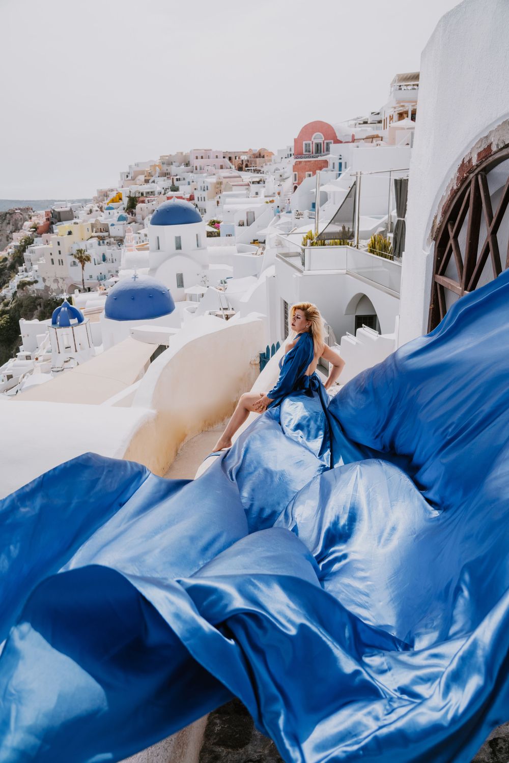 Flowing blue silk dress against whitewashed buildings and blue domes of Santorini.