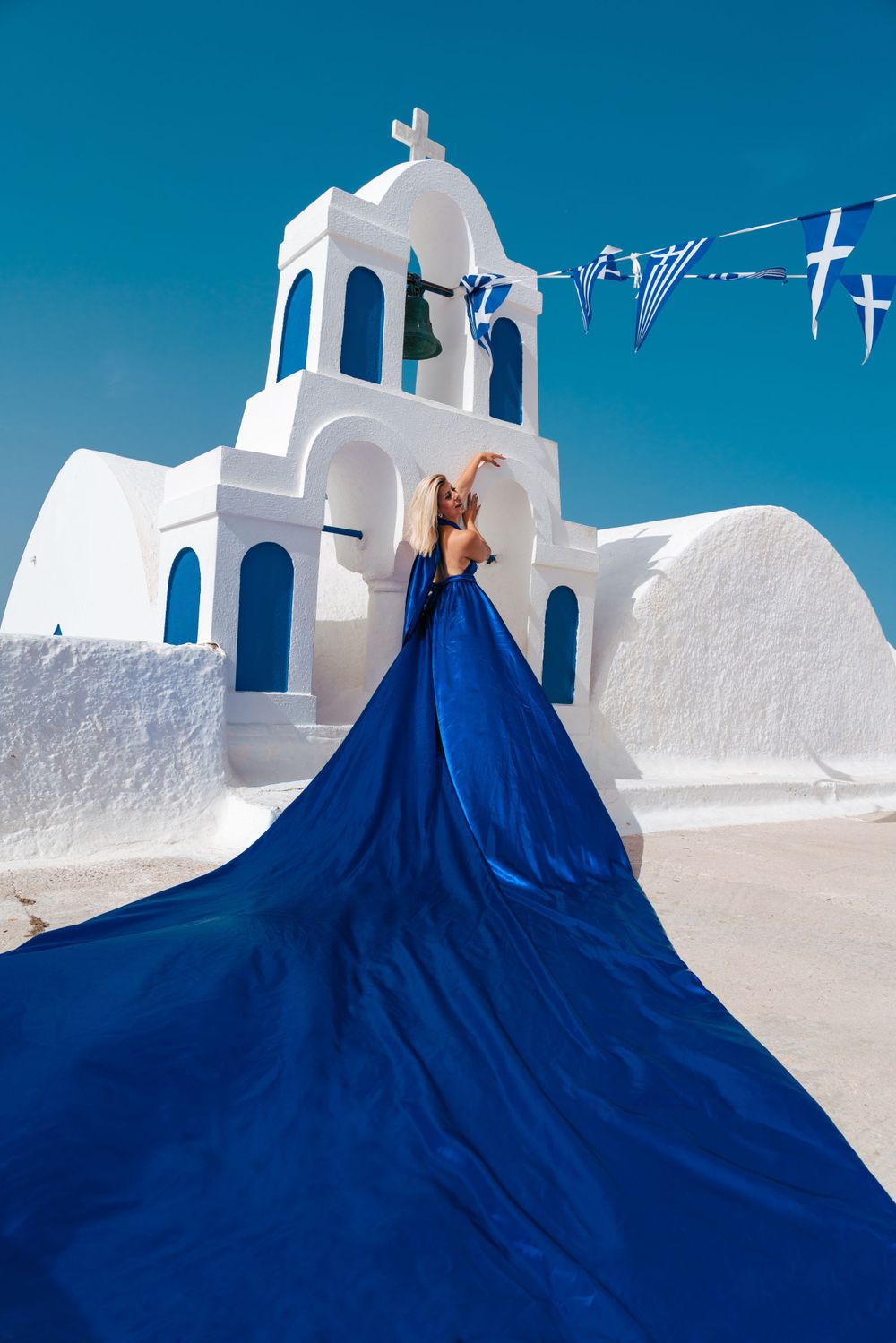 Long blue dress train spreads dramatically in front of white Greek orthodox church.