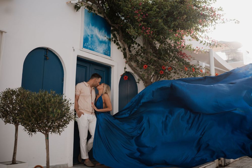 Deep blue flowing fabric creates movement against white Mediterranean architecture and blue doorways.