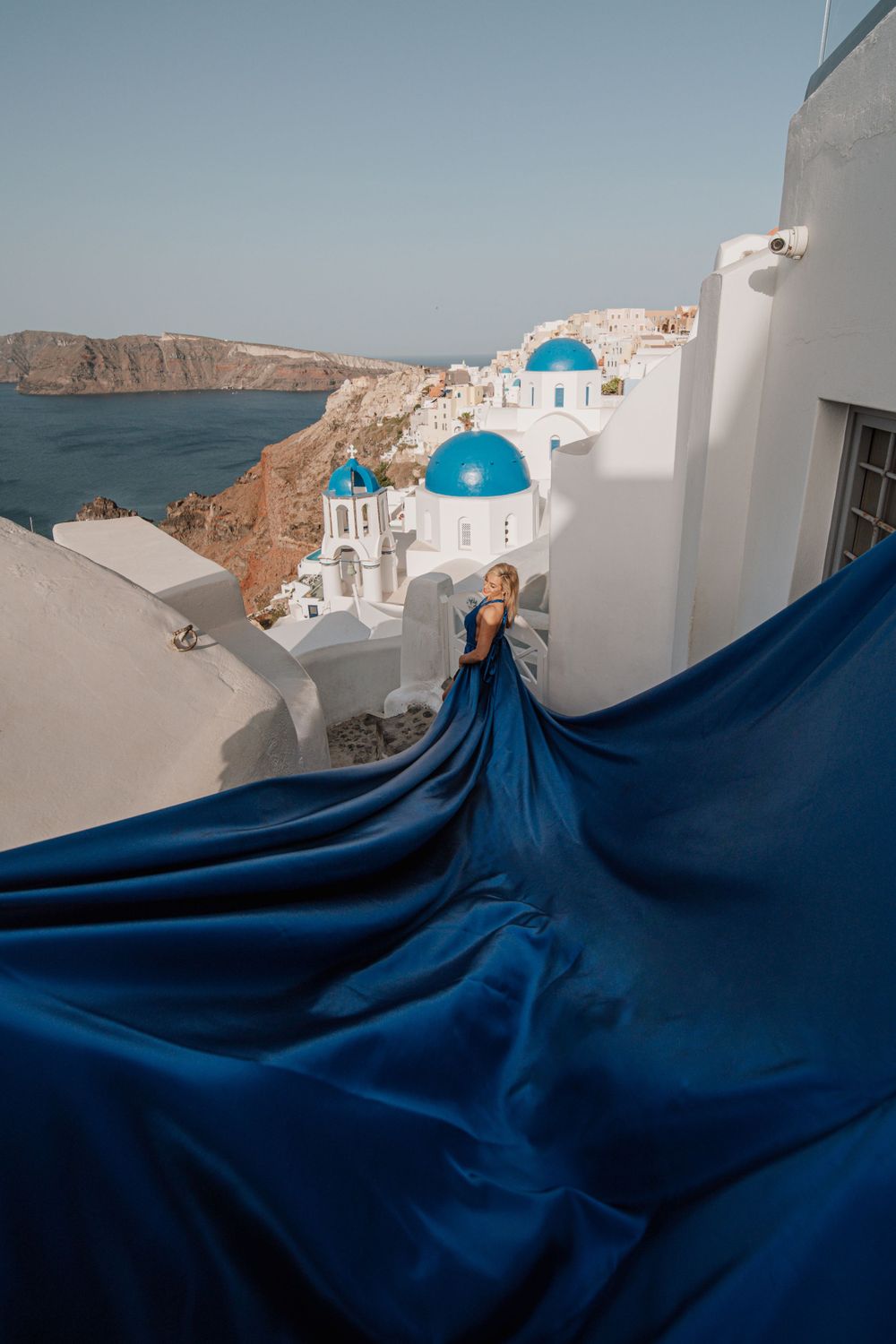 Dramatic blue flowing dress overlooking Santorini's iconic white buildings and blue domed churches.