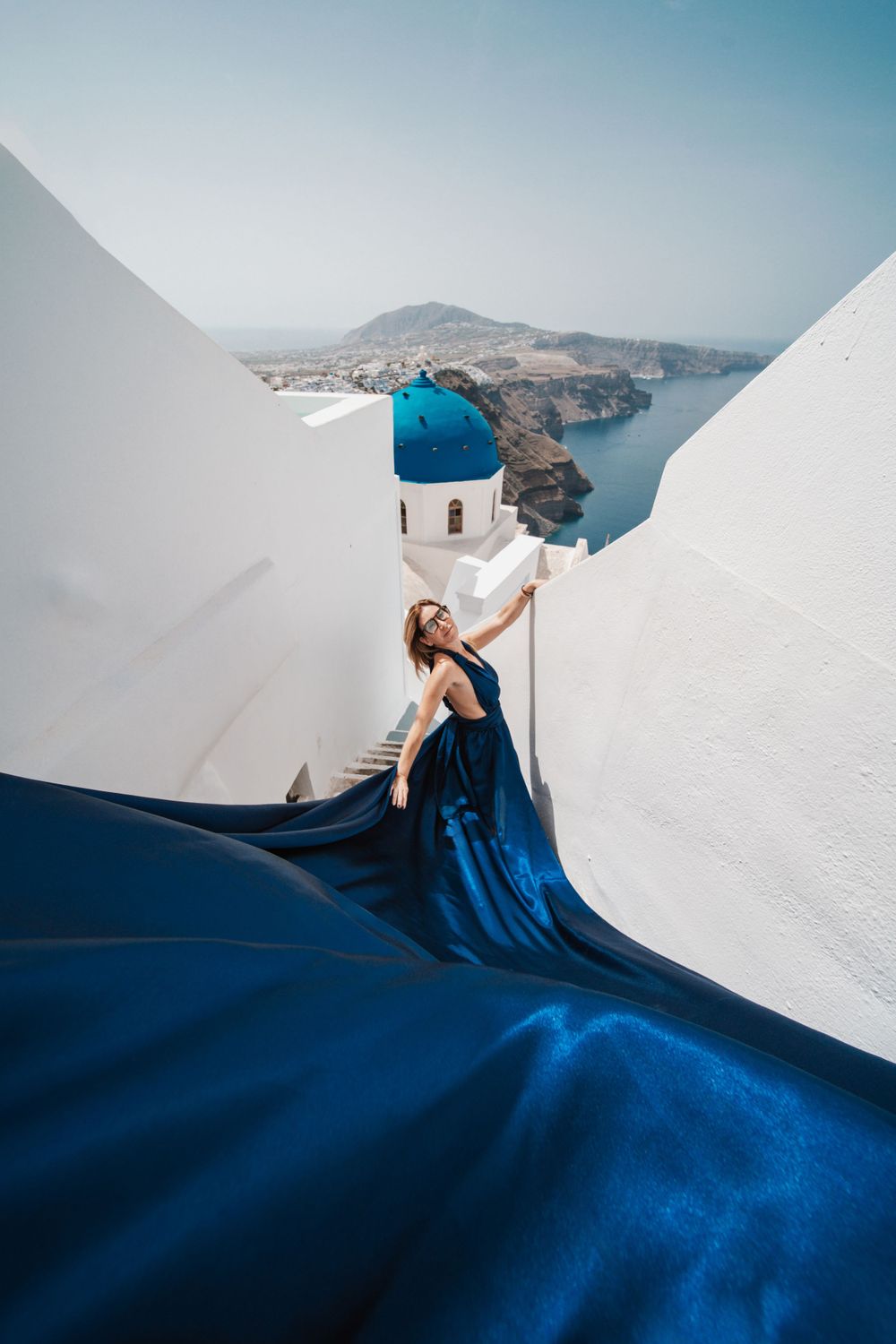 Flowing navy dress against whitewashed walls and blue domed church overlooking Aegean Sea.