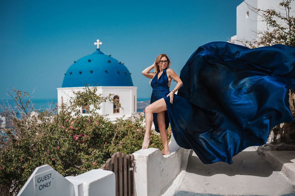 Blue dress billowing in wind against classic Greek church architecture and blue dome.