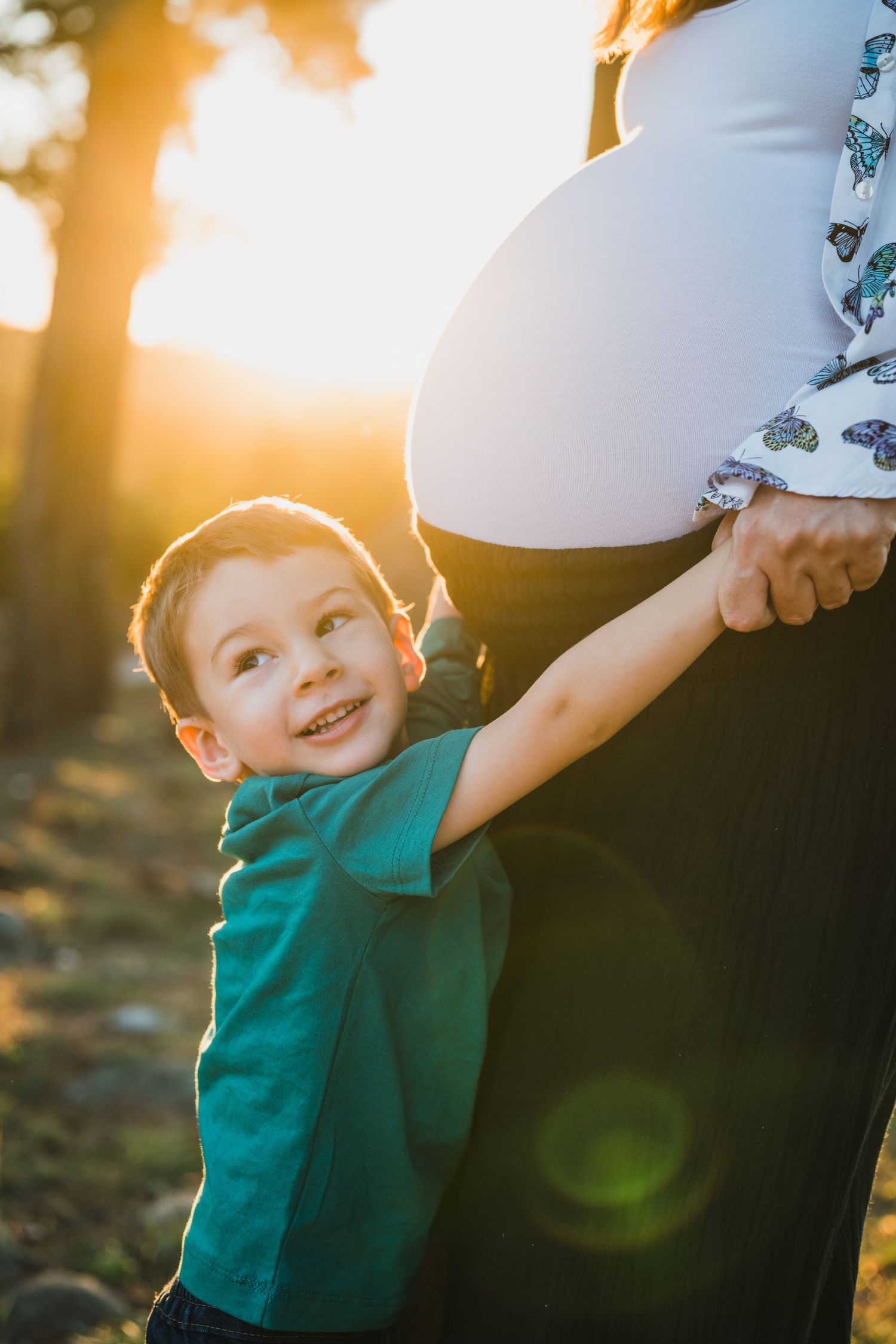 niño abrazando la panza de su madre embarazada al atardecer